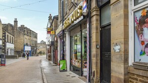 Une vue de rue avec un salon de coiffure, une enseigne verte et un magasin fermé avec un volet noir.