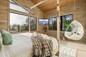 A bedroom with a large bed, a hanging chair, and a TV on the wall. - Epic Views, GameRm+Theatre, HTub, Sauna, 9mi Sunday River (Bethel)