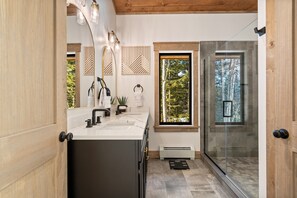 A modern bathroom with a large mirror, two sinks, a shower, and a view of trees through a window. - Epic Views, GameRm+Theatre, HTub, Sauna, 9mi Sunday River (Bethel)