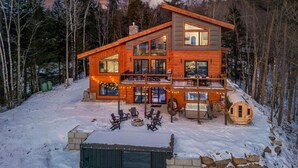 Una baita di legno a due piani con veranda, posti a sedere all'aperto e un braciere.