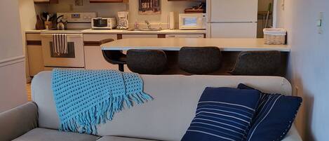 A living room with a sofa, a coffee table, and a kitchen in the background.