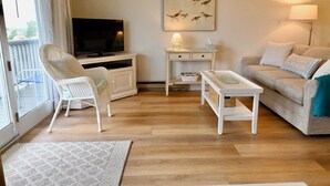 A living room with a television, white furniture, a painting, and a lamp. - Located just steps from Wells Beach, Eastwinds 123 is perfect for your getaway. (Wells)