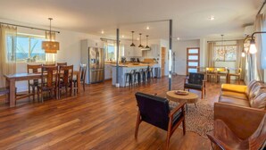A spacious living area with a wooden floor, a dining table with chairs, a sofa, and a kitchen in the background. - Willow Mtn. Ridge: Luxury & seclusion 10mi to BBNP (Terlingua)