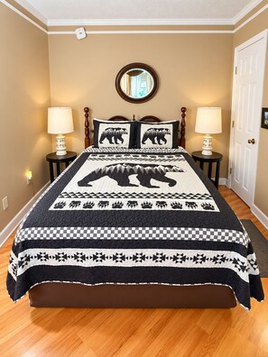 A bedroom with a bed, two bedside tables, a round mirror, and a door.