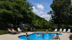 Ein Poolbereich mit mehreren Pools, Liegestühlen und einem eingezäunten Garten.
