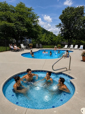 A swimming pool area with multiple pools, lounge chairs, and a fenced garden.