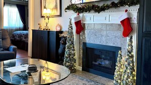 Ein Wohnzimmer mit Kamin, einem darüber montierten Fernseher und Weihnachtsdekorationen, darunter Socken und ein Weihnachtsbaum.
