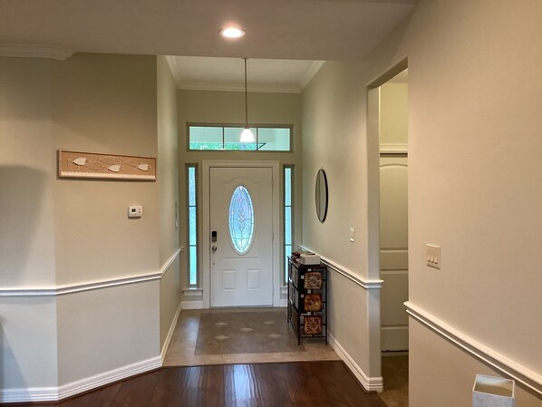 A hallway with a wooden floor, a door with a stained glass window, and a wall-mounted clock.