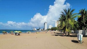 Une plage avec des parasols, des palmiers et des bâtiments en arrière-plan.