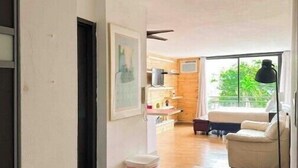 A spacious living area with a wooden floor, a sofa, a dining table, and a kitchen in the background.