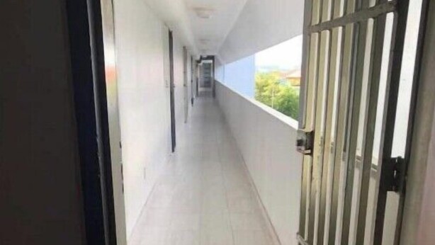Un couloir dont le sol est recouvert de carreaux et qui est bordé d’un côté par des grilles métalliques.