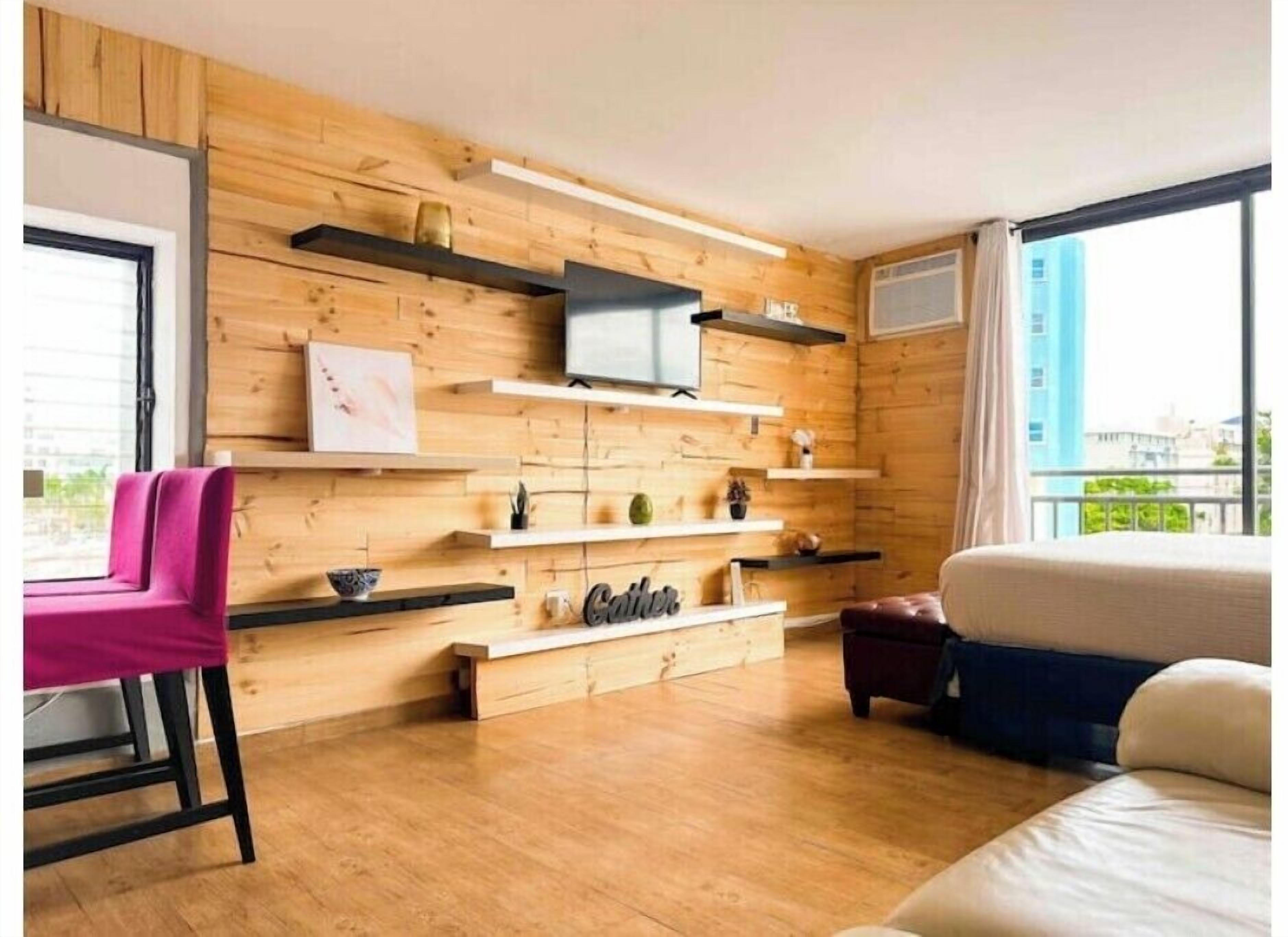 A modern room with wooden panel walls, a flat-screen TV mounted on a shelf, a sofa, a chair, and a bed.