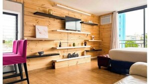 A modern room with wooden panel walls, a flat-screen TV mounted on a shelf, a sofa, a chair, and a bed.