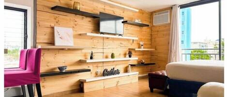 A modern room with wooden panel walls, a flat-screen TV mounted on a shelf, a sofa, a chair, and a bed.