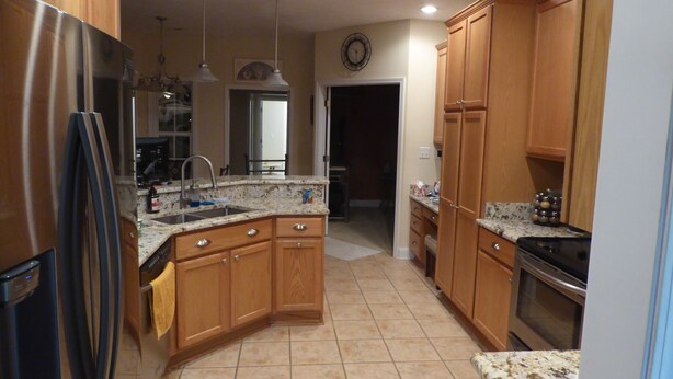 A kitchen with wooden cabinets, a stainless steel refrigerator, a granite countertop, and a built-in oven.