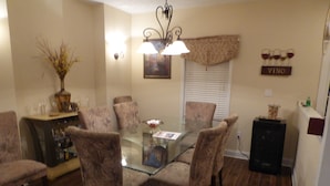 A dining area with a glass-top table surrounded by six upholstered chairs.