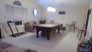 A room with a pool table, a sofa, a dining table with chairs, and a bar area.