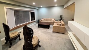 A living room with a sectional sofa, a wooden chair, a coffee table, and a large window with blinds.