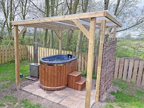 A wooden hot tub under a pergola in a garden setting.