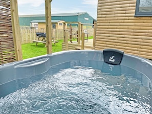 A hot tub with a logo, a wooden deck, and a fenced yard with a building in the background.
