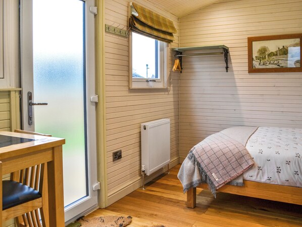 A room with a bed, a window with a curtain, a radiator, a wooden table, and a chair.