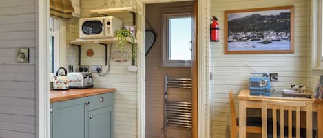 A compact kitchen with a microwave, toaster, and kettle on the counter, a small table with a radio, and a framed picture on the wall.