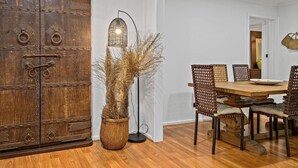 A dining area with a wooden table and chairs, a large rustic cabinet, and a tall floor lamp with a woven shade.