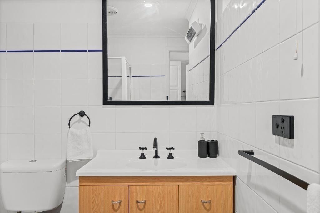 A modern bathroom with a white sink, wooden cabinet, and a large mirror.