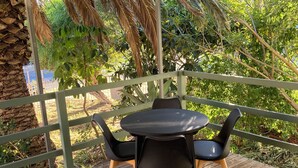 A covered outdoor seating area with a wooden deck, a round table, and black chairs.