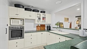 A modern kitchen with white cabinets, a microwave, an oven, a sink, and a green countertop.