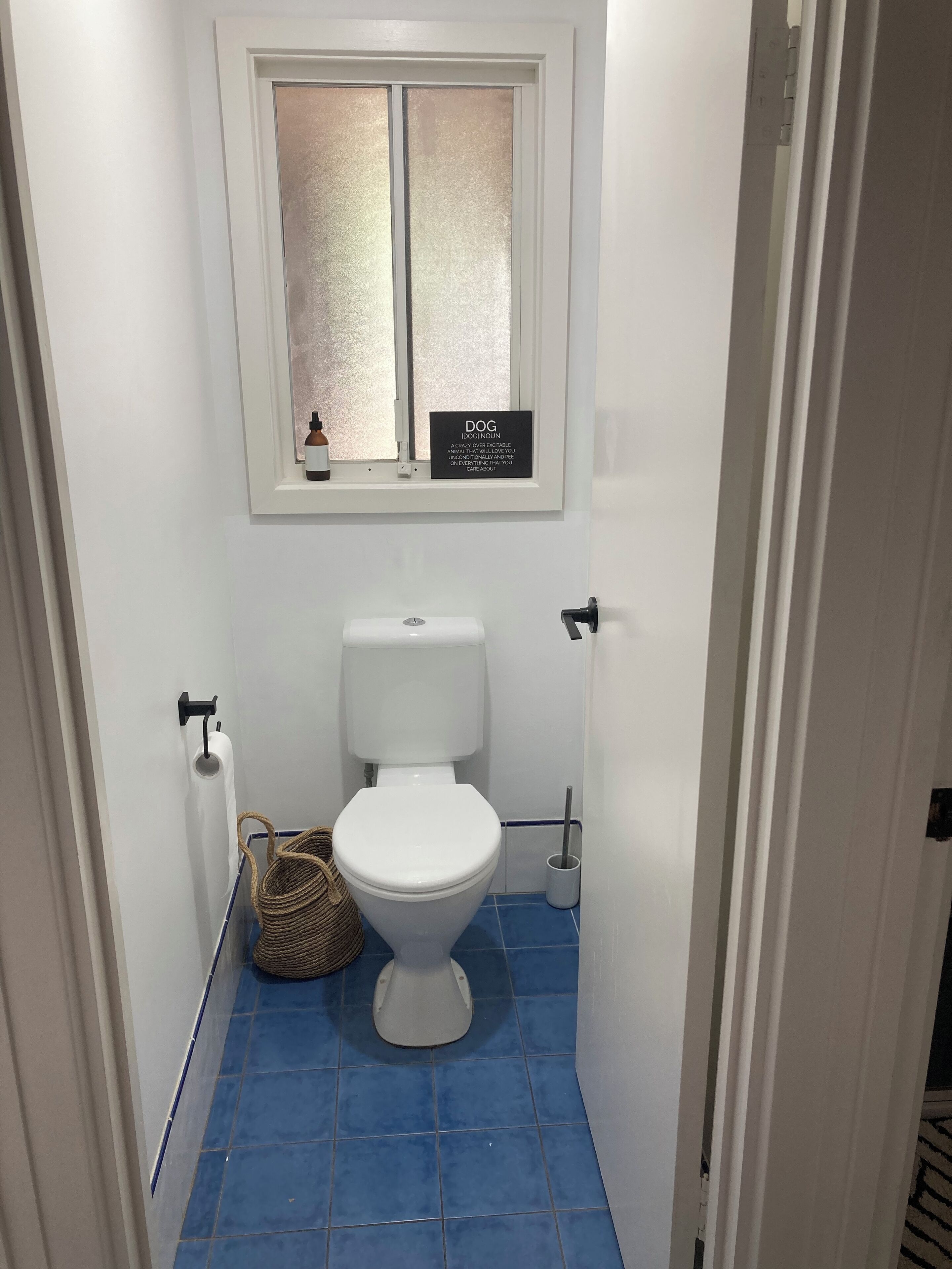 A small bathroom with a white toilet, a window with frosted glass, and a blue-tiled floor.