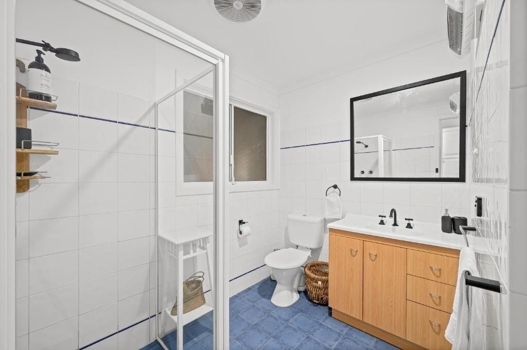 A bathroom with white tiles, a blue floor, a wooden cabinet, a white toilet, and a mirror above the sink.