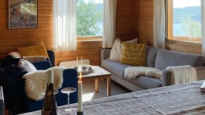 A cozy cabin interior with a sofa, chairs, a table with candles, and a poster on the wall.