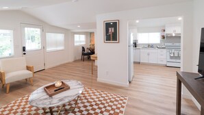 A modern living room with a marble coffee table, a checkered rug, and a sofa. A kitchen with white cabinets and appliances is visible in the background. - Central Thousand Oaks retreat close to shops & eats! (Thousand Oaks)