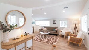 A modern living room with a wooden floor, a round mirror, a sofa, a coffee table, and a dining table. - Central Thousand Oaks retreat close to shops & eats! (Thousand Oaks)