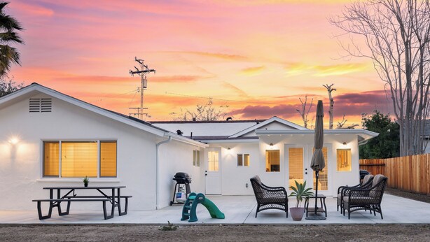 A house with a patio, a picnic table, two wicker chairs, a small table with a table umbrella, a slide, and a wooden fence. - Central Thousand Oaks retreat close to shops & eats! (Thousand Oaks)