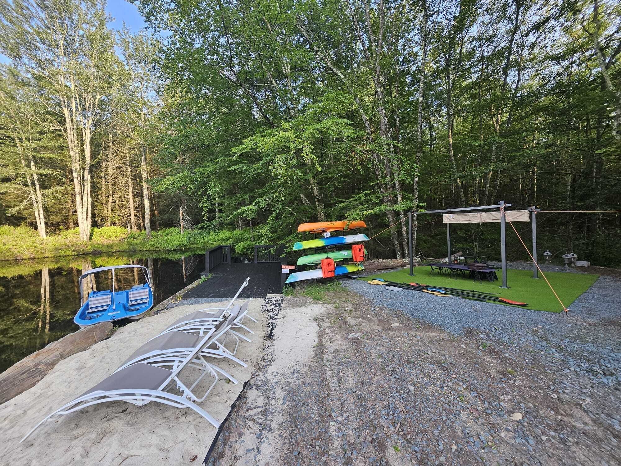 Un terrain de camping situé au bord de la rivière, avec des canoës, un espace de repos couvert et un quai.