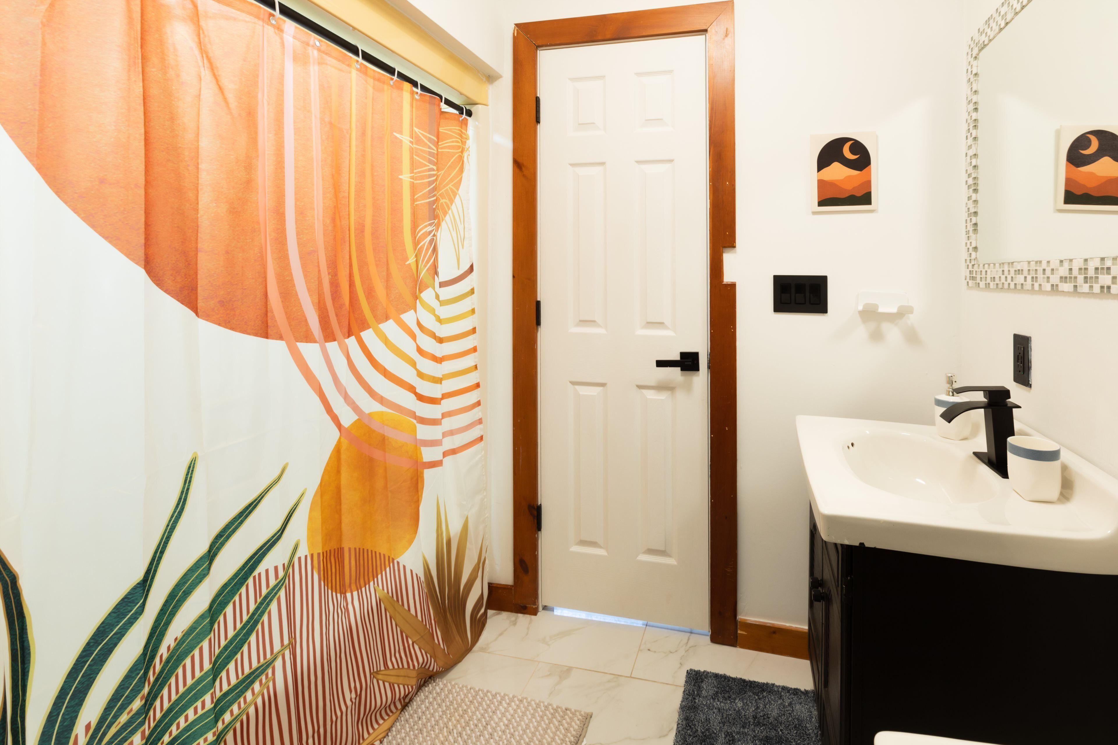 A bathroom with a white door, a sink with a black faucet, and a shower curtain with a tropical design.