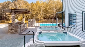 Een achtertuin met een zwembad, twee jacuzzi's en een barbecueplaats van natuursteen.