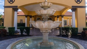 Una fuente de varios niveles en un patio con arcos y columnas, rodeado de setos podados.