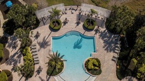 Vista aérea de un resort con una piscina central, rodeado de áreas de descanso y palmeras.