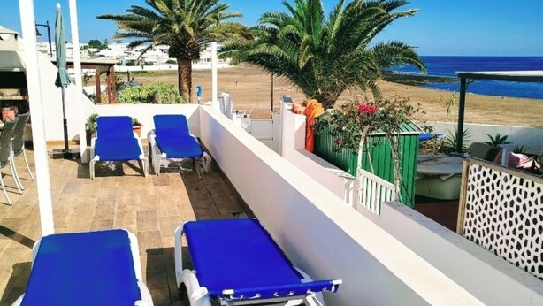 A balcony with blue lounge chairs, a wooden floor, and a view of the beach and ocean. - Dream getaway! seaview shell (Playa Honda , lanzarote)