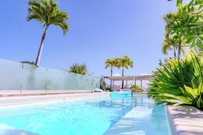 Une piscine à l’eau cristalline, entourée de palmiers et dotée d’un espace abrité.