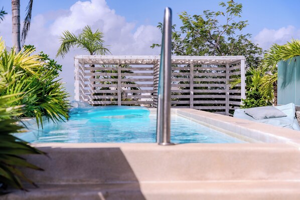 Un espace piscine doté d’une terrasse en bois, de palmiers et surplombant un ciel d’un bleu limpide.