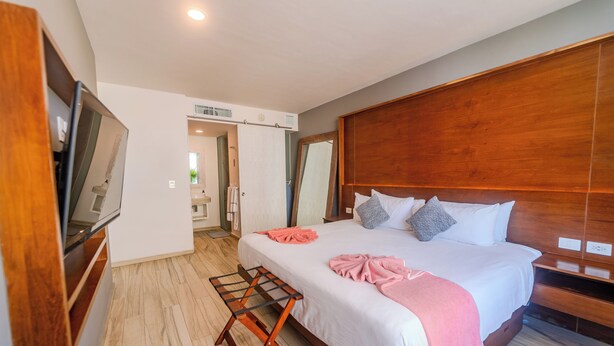 A hotel room with a large bed, wooden headboard, a TV on the left, and a wooden bench at the foot of the bed. - Newport House by Casago (Playa del Carmen)