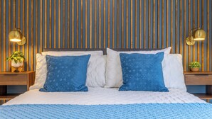 A neatly made bed with two blue patterned pillows, a white duvet, and a blue textured blanket. There are two bedside tables with lamps and small potted plants. The wall behind the bed has vertical wooden slats. - 4 Guest, 5 minutes from all the attractions in Miami,Airport, Downtown, Wynwood (Miami)
