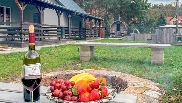A bottle of wine, a glass, and a basket of fruit on a table outdoors with a building and a wooden structure in the background. - Pet friendly home in Ostroda with WiFi (Ostroda)