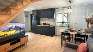 A modern kitchen with dark cabinets, a wooden dining table set for four, and a TV displaying a scenic landscape. - Pet friendly home in Ostroda with WiFi (Ostroda)