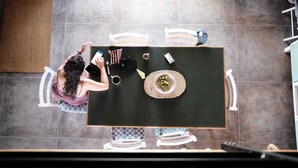 A top-down view of a dining area with a table set for two, a person using a smartphone, and various items on the table including a cup, a small bowl, and a bag.