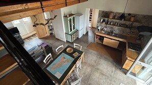 A loft-style bedroom with a bunk bed, a dining area with a map, a kitchen with a stone backsplash, and a view of the outside.